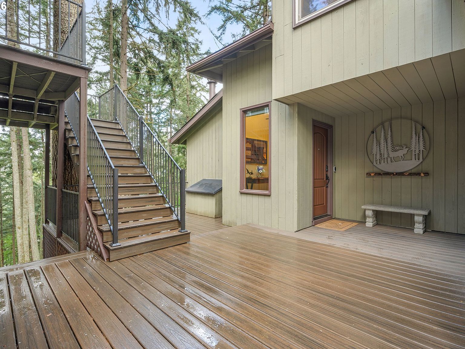 Expansive Trex deck at 4330 N Shasta Loop wrapping the back of the home, with a steel-railing stair descending into the surrounding canopy of Douglas firs on the private wooded acre